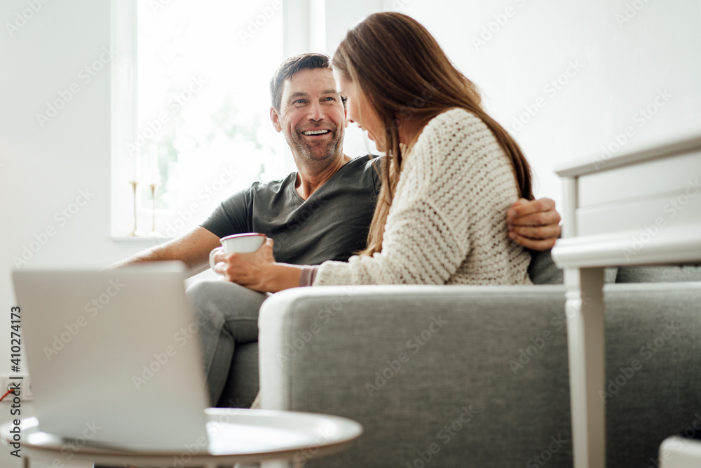 Cheerful mature couple laughing while sitting on sofa at home Cheerful mature couple laughing while sitting on sofa at home