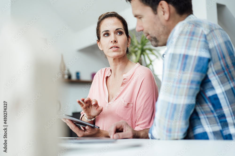 Mature woman with digital tablet looking at man in apartment Mature woman with digital tablet looking at man in apartment