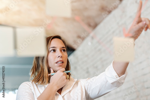 Businesswoman planning over adhesive notes stuck on glass wall in office