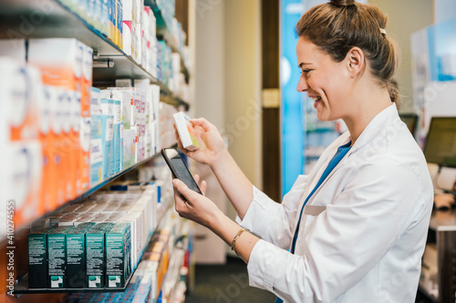 Happy pharmacist with smart phone checking medicine while working at pharmacy