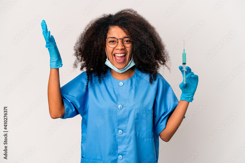 Young african american curly doctor woman holding a syringe receiving a pleasant surprise, excited and raising hands. Young african american curly doctor woman holding a syringe receiving a pleasant surprise, excited and raising hands.