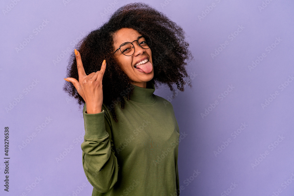 Young african american curly woman isolated on purple background showing rock gesture with fingers Young african american curly woman isolated on purple background showing rock gesture with fingers