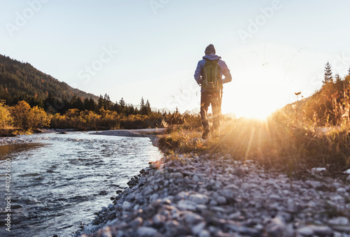 Male hiker with backpack walking on land by stream against clear sky at sunset photo