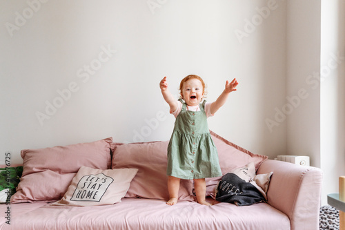 Smiling baby girl standing on sofa with arms raised