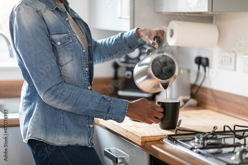 Woman pouring water from kettle into mug in kitchen photo