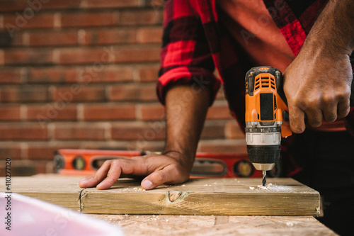 Midsection of man using drill machine on plank while renovating during summer