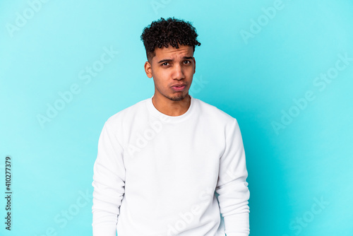 Young african american curly man isolated on blue blows cheeks, has tired expression. Facial expression concept.