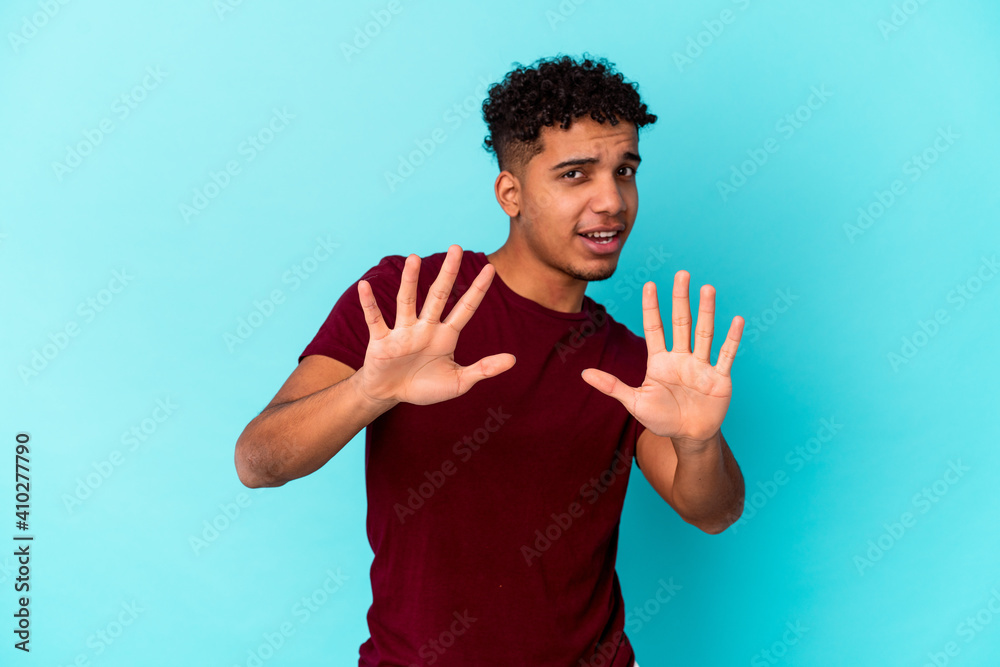Young african american curly man isolated on blue rejecting someone showing a gesture of disgust. Young african american curly man isolated on blue rejecting someone showing a gesture of disgust.