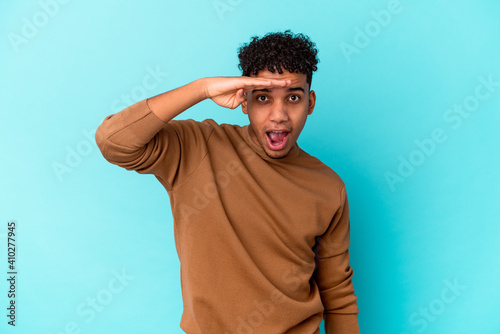 Young african american curly man isolated on blue looking far away keeping hand on forehead.
