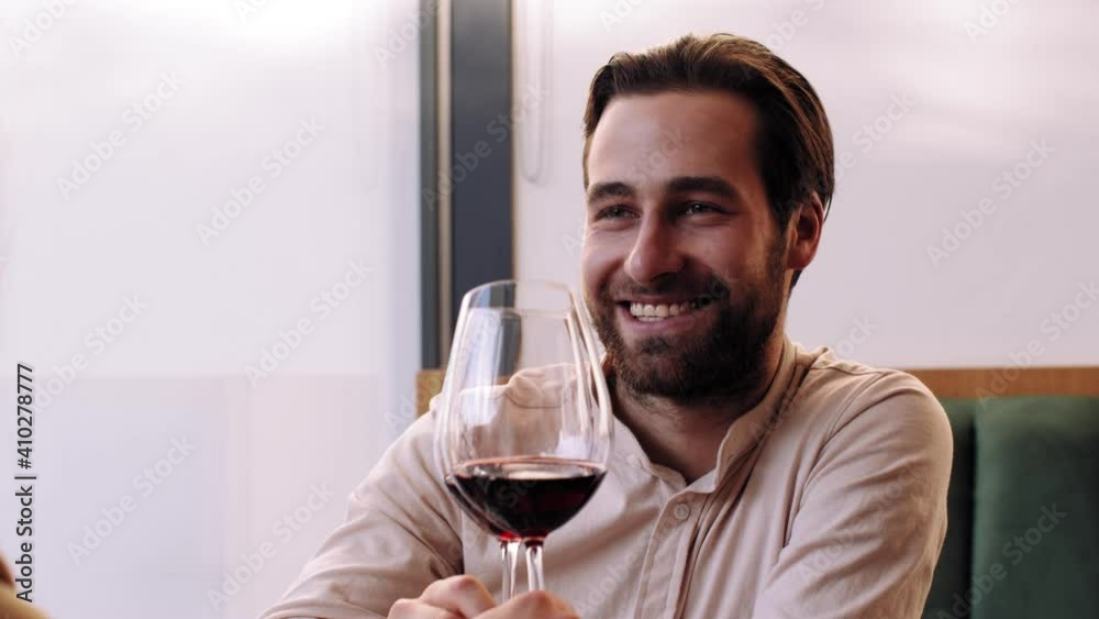 Happy man saying toast and clinking wine glasses with his girlfriend, enjoying romantic date in cafe, slow motion Happy man saying toast and clinking wine glasses with his girlfriend, enjoying romantic date in cafe, slow motion