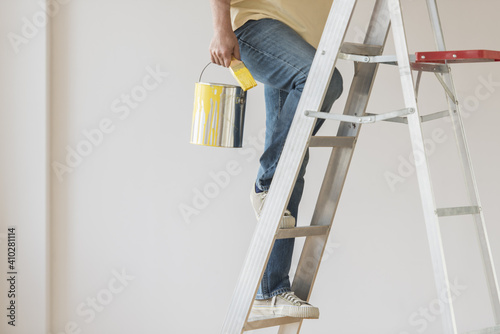 Man holding paint can and climbing ladder