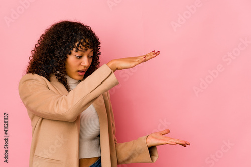 Young african american afro woman isolated shocked and amazed holding a copy space between hands.