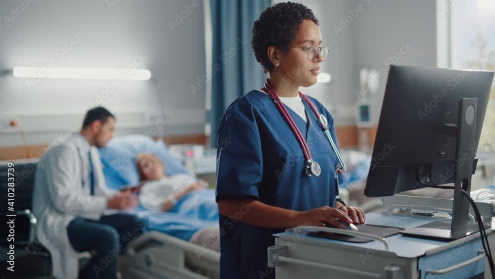 Hospital Ward: Professional Black Female Head Nurse Uses Medical Computer. In the Background Modern Equipment Clinic Doctor Consulting Patient Recovering After Successful Surgery in Bed