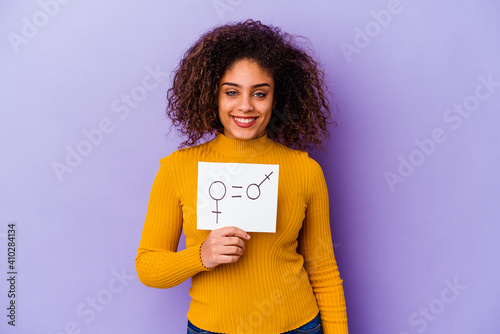 Young African American woman holding a gender equality placard isolated on purple background happy, smiling and cheerful.