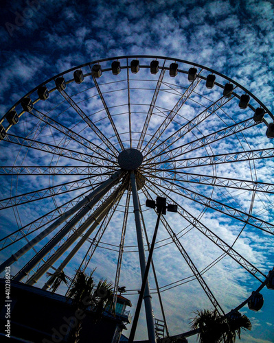 tall Ferris wheel at carnival from ground during the day with beautiful blue and cloudy sky looking up, vertical