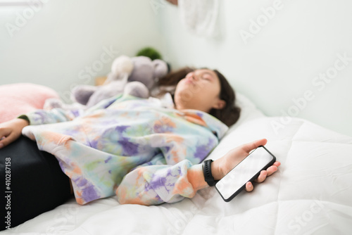 Teenage girl dozing off in bed with a phone on her hand