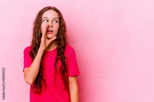 Little caucasian girl isolated on pink background is saying a secret hot braking news and looking aside