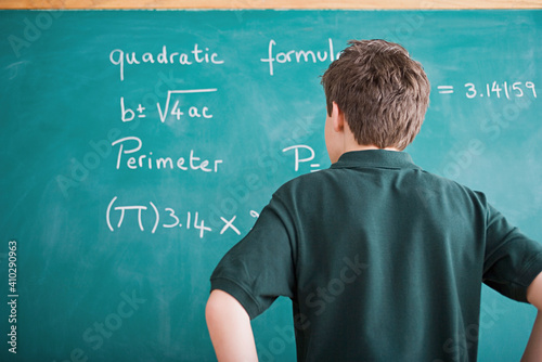 Boy standing in front of blackboard looking at mathematical formula photo