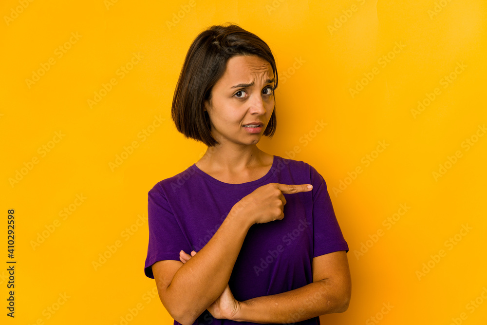 Young hispanic woman isolated on yellow smiling and pointing aside, showing something at blank space. Young hispanic woman isolated on yellow smiling and pointing aside, showing something at blank space.