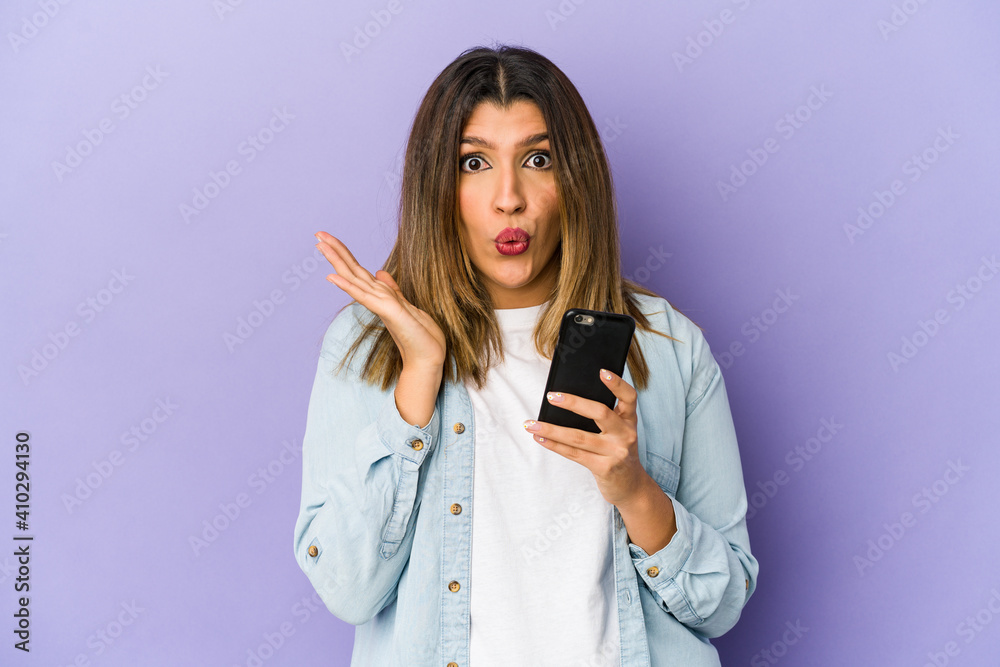 Young indian woman holding a phone isolated surprised and shocked. Young indian woman holding a phone isolated surprised and shocked.