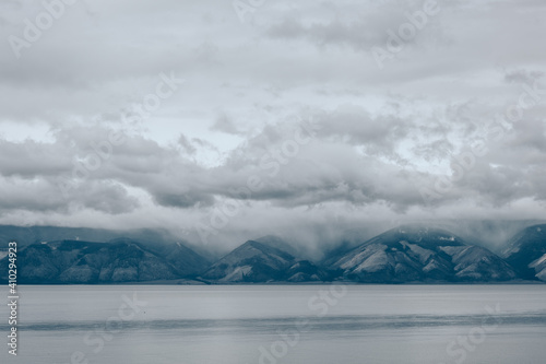 Dramatic clouds over the lake and in the mountains. Gray foggy morning, cloudy weather. Lake Baikal, Russia.