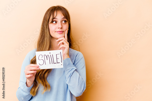 Young caucasian woman holding a Smile placard isolated looking sideways with doubtful and skeptical expression.