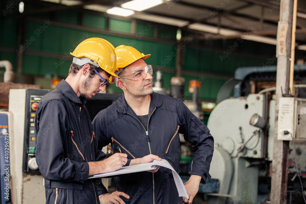 Two workers at an industrial. technician engineer checking process on notebook to machinery in factory. workers using machine equipment in factory Two workers at an industrial. technician engineer checking process on notebook to machinery in factory. workers using machine equipment in factory