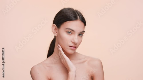 Medium close-up beauty portrait of Young slim woman who gently touches and strokes her jawline and look at the camera | Beauty and skin care concept