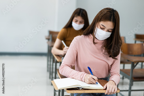 Group of college students wearing a face mask and keep distance while studying in the classroom and college or university campus to prevent COVID-19 pandemic. The new college or university campus life