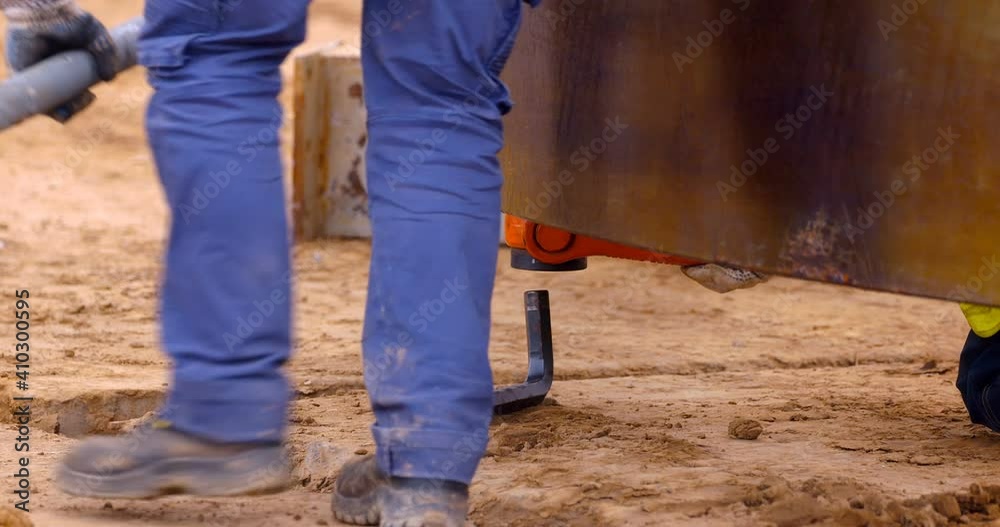 On a construction site, a worker uses a pipe and a huge hex key to tighten the mount for lifting the part with a crane On a construction site, a worker uses a pipe and a huge hex key to tighten the mount for lifting the part with a crane
