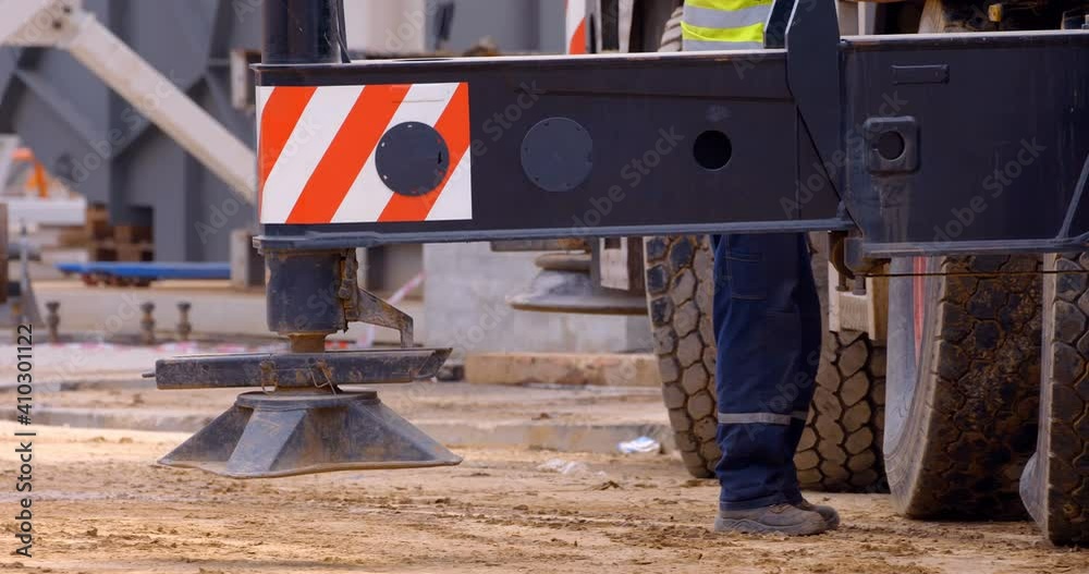 At a construction site, a multi-axle powerful mobile crane is preparing to lift a load, operator extends outriggers for work