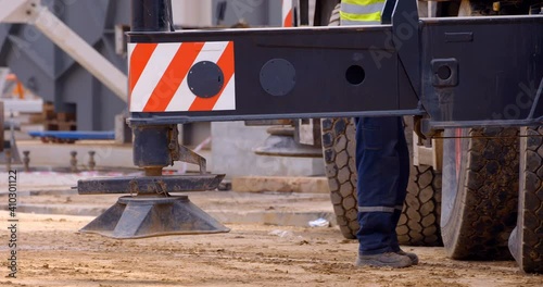 At a construction site, a multi-axle powerful mobile crane is preparing to lift a load, operator extends outriggers for work