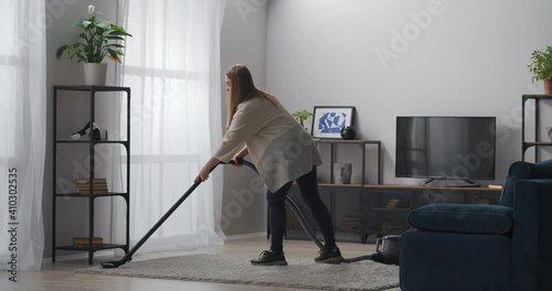 cleaning carpet by vacuum cleaner, woman is doing housework in modern apartment, household appliances photo