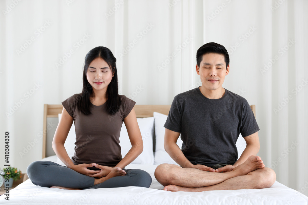 Man and woman Buddhist sitting on bed in the bedroom and doing meditation in Buddhism religion style together. The idea for faith and trust in religion and calm of mind Man and woman Buddhist sitting on bed in the bedroom and doing meditation in Buddhism religion style together. The idea for faith and trust in religion and calm of mind