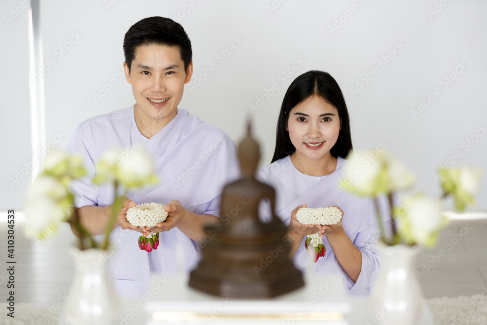 Man and woman Buddhist in white dress sitting in front of set of altar table and paying homage to buddha image. Idea for ritual and faith and calm of mind Man and woman Buddhist in white dress sitting in front of set of altar table and paying homage to buddha image. Idea for ritual and faith and calm of mind