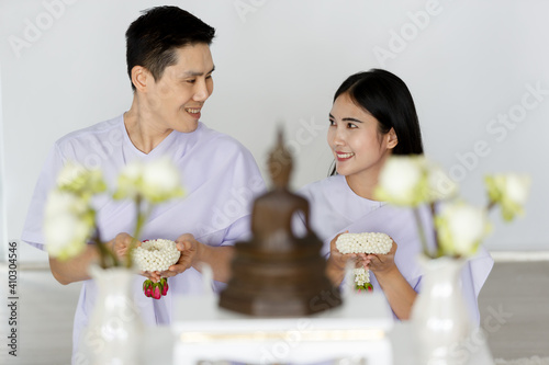 Man and woman Buddhist in white dress sitting  in front of set of altar table and paying homage to buddha image. Idea for ritual and faith and calm of mind