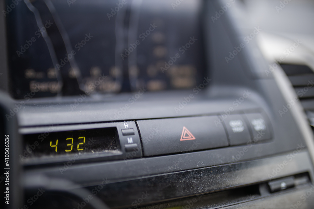 Emergency blinkers button and digital clock on dusty car dashboard