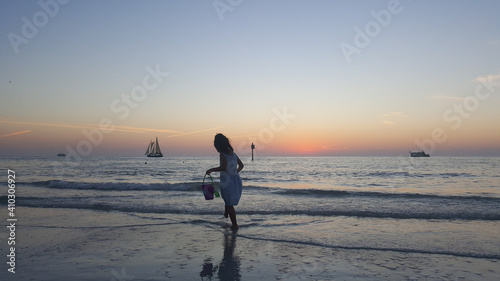 little girl with a watering can is playing at the beach during a sunset