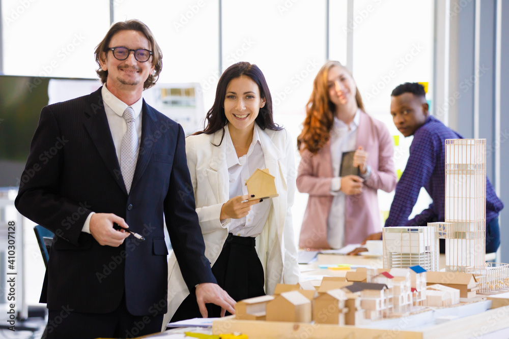 A man caucasian manager and young businesswoman picks up a house model to take pictures to promote real estate in the office. Concept business promote. A man caucasian manager and young businesswoman picks up a house model to take pictures to promote real estate in the office. Concept business promote.