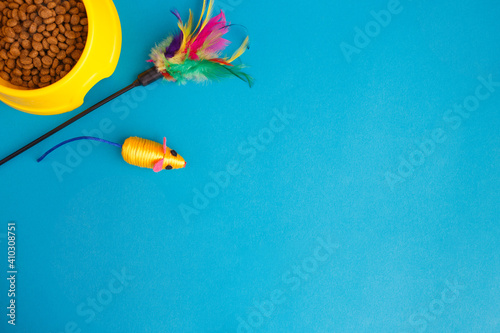 Set of accessories for the cat on blue background. Yellow bowl, mouse, toy. Caring concept. Feline background. Top view, flat lay