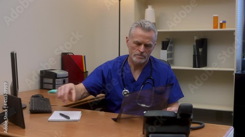 Concerned male doctor examines chest x-ray of sick patient takes notes and sends an email