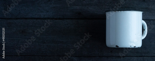 White empty enamel mug, on a wooden background.
