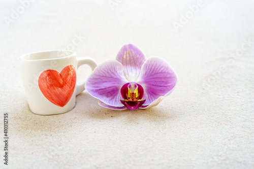 cup coffee with red heart printed and blossom phaleanopsis orchid on sandy background.
 photo