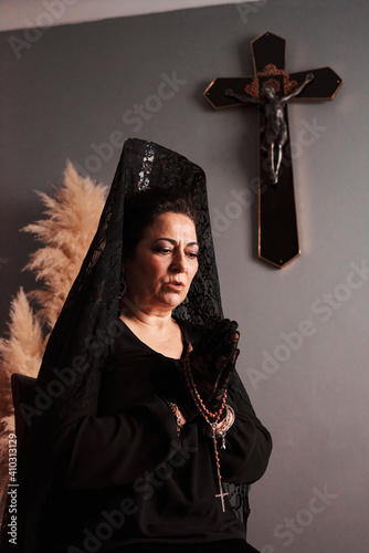 A woman in a mantilla praying with a rosary in her hands photo