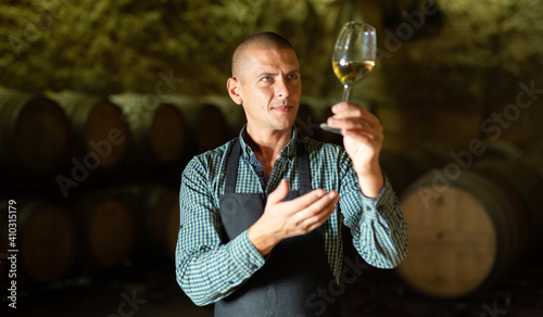 Fotografia Confident winemaker inspecting quality of white wine, standing in front of woode