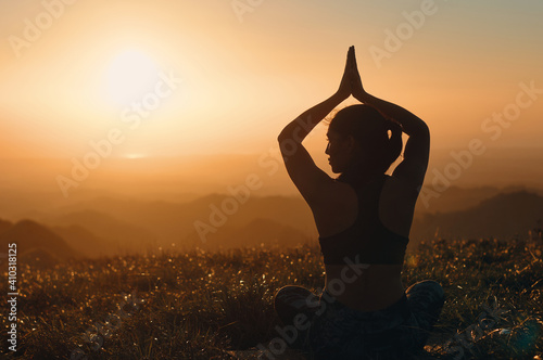 Back view of woman's silhouette that practices yoga in nature. Lotus pose with her hands over her head