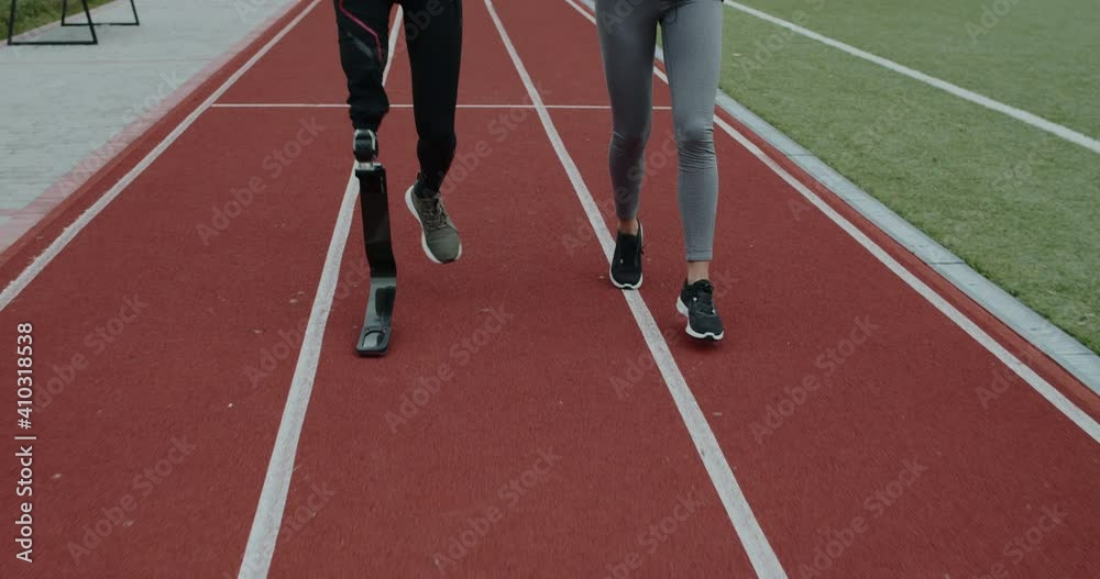 Crop view of disabled man with amputated leg and sports woman jogging. Male sportsman with running blade and female person run on race track at stadium. Concept of motiation, health, sports. Crop view of disabled man with amputated leg and sports woman jogging. Male sportsman with running blade and female person run on race track at stadium. Concept of motiation, health, sports.