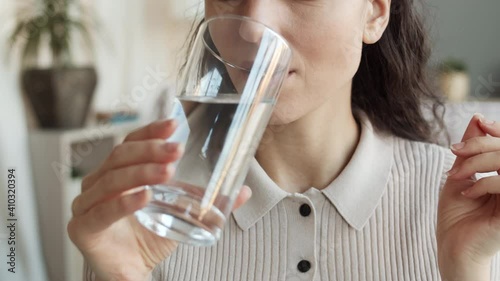 Close-up of cropped unrecognizable woman holding vitamin pill and glass of water, then taking medicine, drinking and smiling