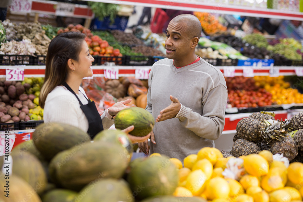 Latin man in fruit section of supermarket with shop worker helping him