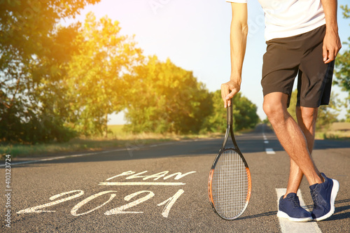 Sporty young man with tennis racket outdoors. Concept of goal achievement